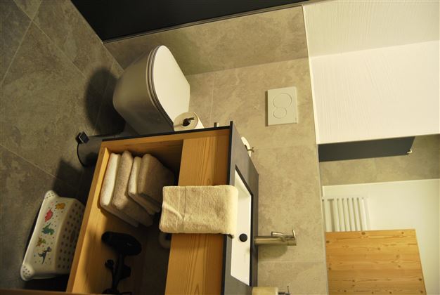 A modern bathroom with a white toilet and a sink. On the cabinet lie folded towels and there is a bright wall.