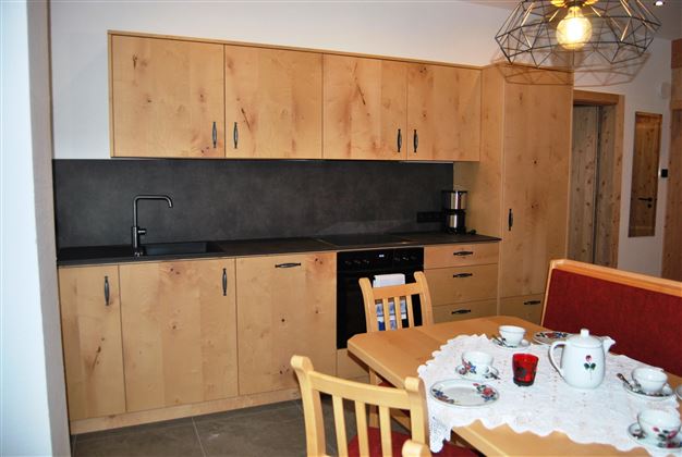 A modern kitchen with wooden-colored cabinets and a black workspace. On the table, there is a teapot and cups for a cozy tea time.