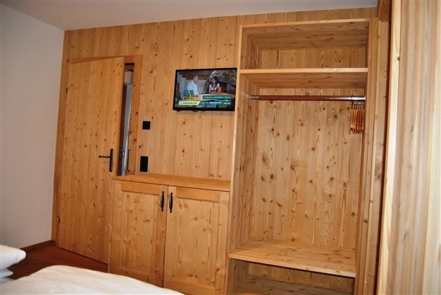 A cozy room with wood paneling and a TV. There is a wardrobe and a table.