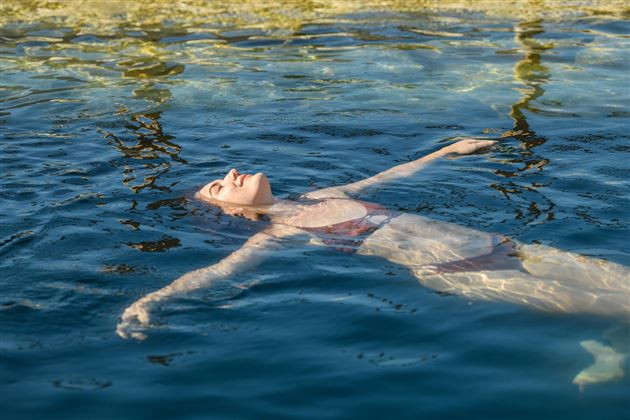 Eine Frau liegt entspannt im Wasser und genießt die Ruhe. Das Licht spiegelt sich sanft auf der Wasseroberfläche.