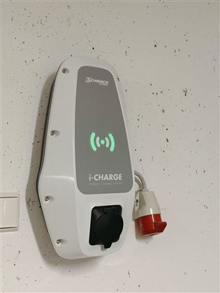 A wall box for charging electric vehicles. It is mounted on a wall and shows a green light.
