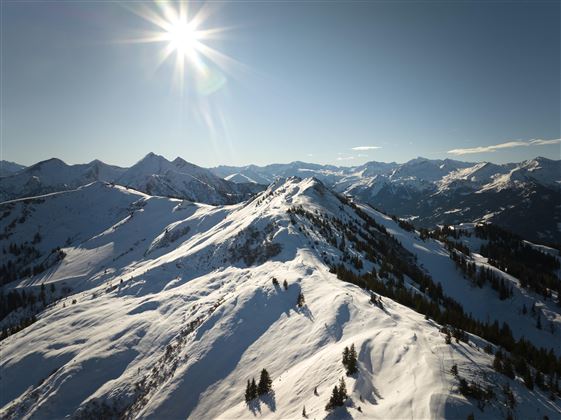 Eine winterliche Berglandschaft mit schneebedeckten Gipfeln und strahlendem Sonnenschein. Der Himmel ist klar und die Aussicht ist atemberaubend.