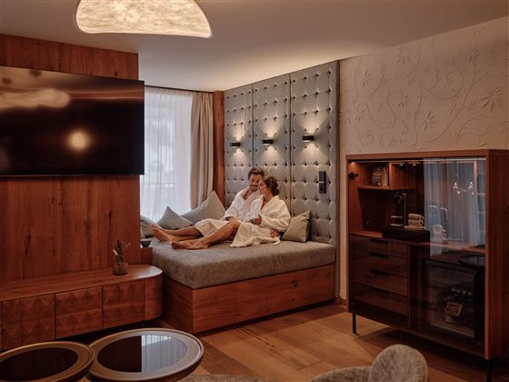 Ein elegantes Zimmer mit einem gemütlichen Bett und modernem Mobiliar. Eine Person in einem Bademantel entspannt in der Wohlfühlatmosphäre.