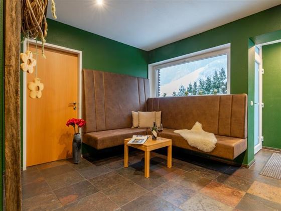 A cozy entrance area with green walls and comfortable benches. The room is decorated with a small table and a lovely view of the landscape.