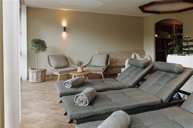 Ein entspannender Wellnessbereich mit gemütlichen Liegen und modernen Möbeln. Pflanzen und sanftes Licht schaffen eine ruhige Atmosphäre.