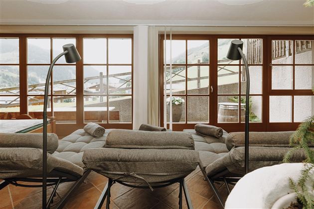Ein modernes Wohnzimmer mit gemütlichen Liegen und großen Fenstern. Der Blick auf die Berge und das natürliche Licht sorgen für eine einladende Atmosphäre.