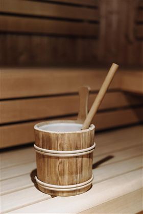 Ein Holzbehälter mit einem langen Löffel steht auf einer Saunabank. Die Umgebung ist warm und einladend, typisch für eine Sauna.