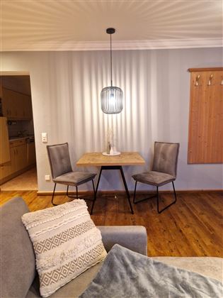 Ein gemütlicher Essbereich mit einem runden Tisch und zwei Stühlen. Über dem Tisch hängt eine moderne Lampe, und der Boden ist aus Holz.