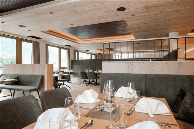 Ein modernes Restaurant mit stilvoll gedeckten Tischen. Große Fenster sorgen für viel Tageslicht und eine gemütliche Atmosphäre.