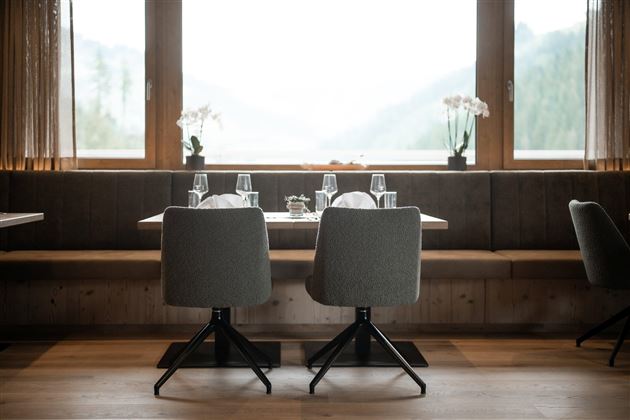 Ein eleganter Restaurantbereich mit einem Tisch für zwei Personen. Die große Fensterfront bietet einen Blick auf die Natur draußen.