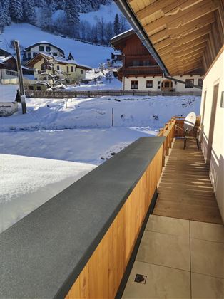 A balcony with a view of snow-covered houses and mountains. The surroundings are calm and wintry.