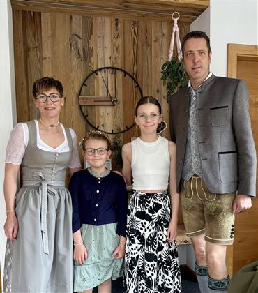 Eine Familie in traditioneller bayerischer Tracht steht in einem gemütlichen Raum. Sie lächeln freundlich und posieren für das Foto.