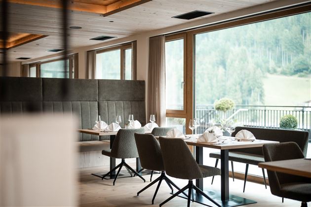 Ein elegantes Restaurant mit modernen Tischen und Stühlen. Große Fenster bieten eine Aussicht auf die grüne Landschaft.