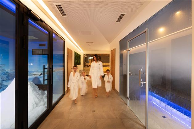 A woman with several children in bathrobes walks through a modern wellness area. The atmosphere is relaxed and inviting.