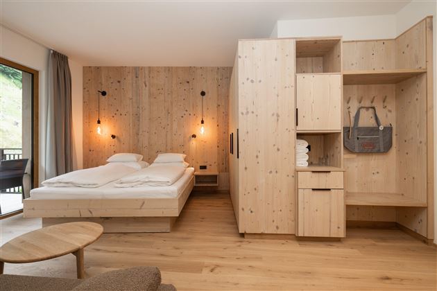 Ein modernes Zimmer mit Holzwänden und einem gemütlichen Doppelbett. Die Einrichtung ist schlicht und angenehm, mit einem Schrank und einem kleinen Tisch.