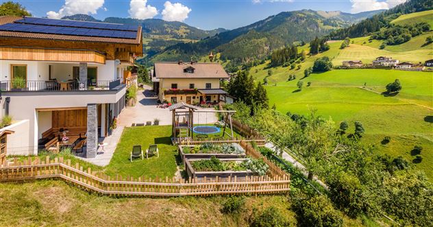 Ein malerisches Grundstück mit modernen Häusern und einem Garten. Die Umgebung ist grün und von Bergen umgeben, unter einem klaren Himmel.