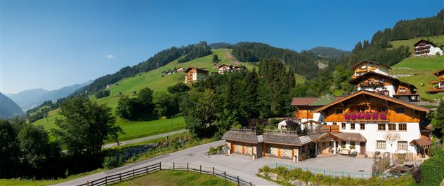 Eine malerische Alpenlandschaft mit grünen Hügeln und traditionellen chalets. Im Vordergrund ein gemütliches Haus mit blühenden Balkonpflanzen.