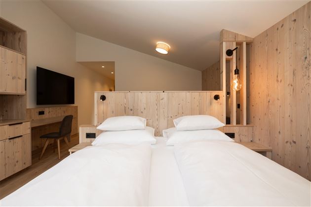Ein modernes Hotelzimmer mit zwei Betten und natürlichem Holzdekor. Der Raum ist hell und freundlich gestaltet, mit einem Fernseher und stilvollen Lampen.
