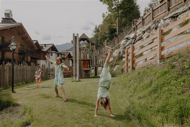 Zwei Kinder spielen fröhlich im Garten. Eines macht einen Handstand, während das andere auf der Wiese steht.