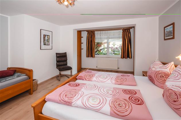 A cozy bedroom with two beds and colorful bedspreads. The windows let in light and the room has a friendly atmosphere.