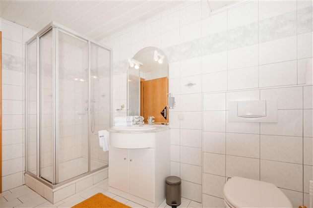 A modern bathroom with white tiles and a shower. There is a sink, a mirror, and a toilet.