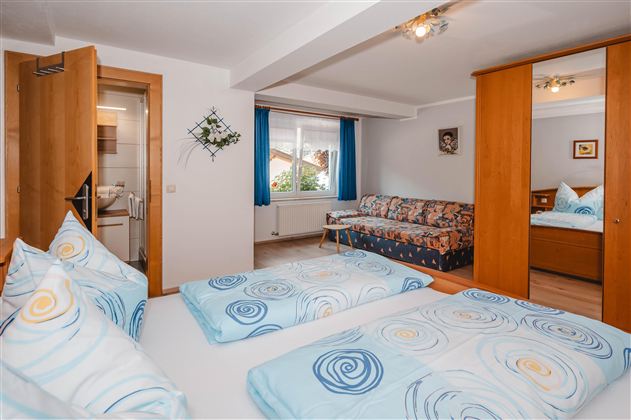 A cozy bedroom with two beds and colorful bedspreads. The room features a window with curtains and a couch.