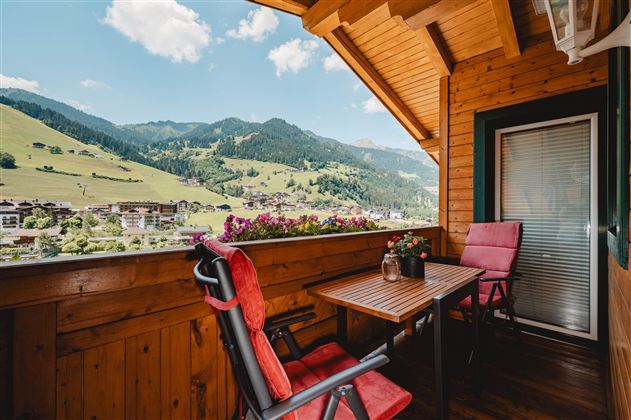 A cozy balcony with a view of green hills and mountains. The table and chairs invite you to relax.