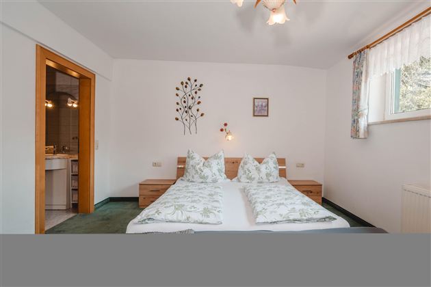 A stylish bedroom with a double bed and decorative cushions. The room has a bright, friendly atmosphere with easy access to the bathroom.