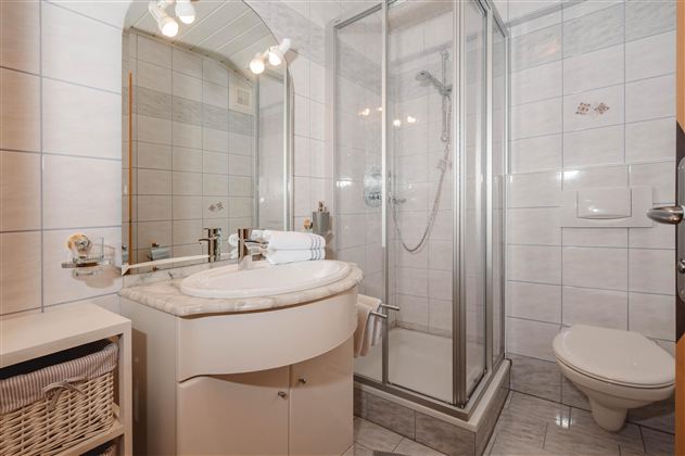 A modern bathroom with a glass shower and a sink. The walls are tiled and there is a large mirror.