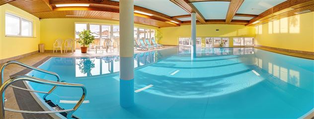 A bright indoor pool with clear water and a friendly yellow hue. There are lounges and windows that provide plenty of daylight.