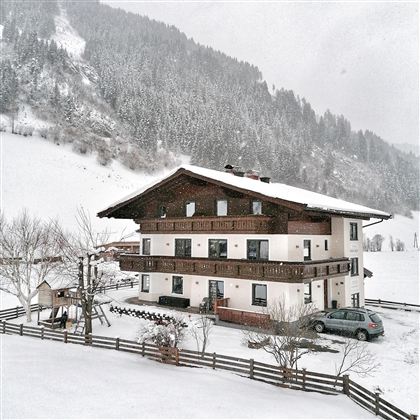 A charming house in the snow with traditional architecture. The surroundings are surrounded by snow-covered mountains and trees.