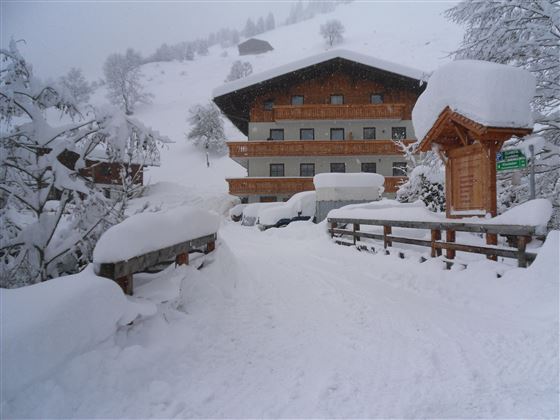 Ein schneebedecktes Gebäude in einer winterlichen Landschaft. Die Umgebung ist ruhig und idyllisch mit dicken Schneeverwehungen.