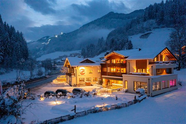 Ein gemütliches Hotel in einer verschneiten Landschaft. Die Lichter des Hotels strahlen in der Dämmerung und schaffen eine einladende Atmosphäre.
