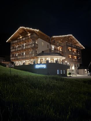 Ein modernes Hotelgebäude in malerischer Umgebung, beleuchtet von warmem Licht. Die Fassade ist einladend und freundlich gestaltet.