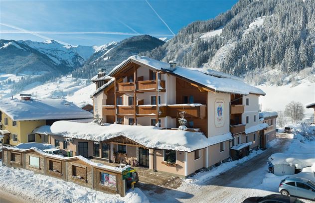 A cozy hotel in the snow with large windows and balconies. In the background, snow-covered mountains can be seen.