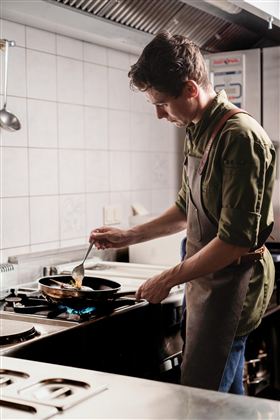 Ein Koch bereitet eine Mahlzeit in einer modernen Küche vor. Er steht am Herd und rührt in einer Pfanne.