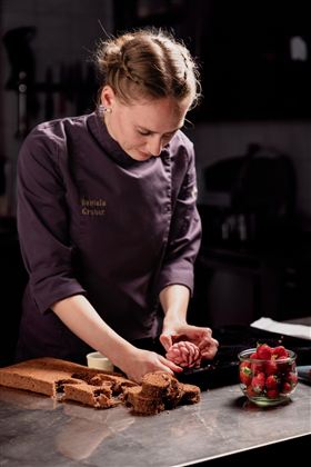 Eine Bäckerin formt mit ihren Händen eine Teigmasse in der Küche. Auf dem Tisch liegt ein Stück Biskuit und eine Schüssel mit frischen Erdbeeren.
