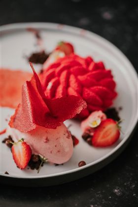 Ein kunstvoll angerichtetes Dessert mit Erdbeersorbet und frischen Erdbeeren. Die Präsentation umfasst auch dekorative Elemente aus Fruchtleder.