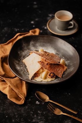 Ein schön angerichteter Dessertteller mit knusprigen Waffeln und einer cremigen Füllung. Dazu liegt eine braune Serviette und eine Tasse Kaffee auf dem Tisch.