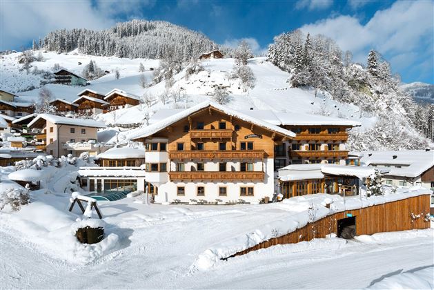 Ein schönes Hotel in einer verschneiten Berglandschaft. Die Umgebung ist winterlich mit schneebedeckten Hügeln und traditionellen Chalets.