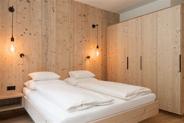 Ein modernes Schlafzimmer mit einem Doppelbett und Holzverkleidung. Die Wände sind aus hellem Holz, und es gibt stilvolle Wandlampen.