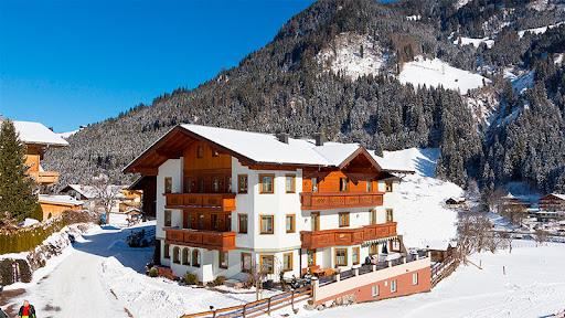 Ein malerisches Chalet inmitten einer verschneiten Landschaft. Im Hintergrund erheben sich schneebedeckte Berge unter einem klaren blauen Himmel.