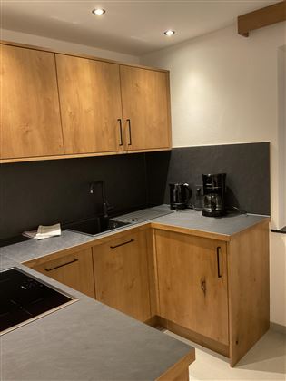 Eine moderne Küche mit Holzschränken und grauen Arbeitsflächen. Auf der Arbeitsplatte stehen ein Wasserkocher und eine Kaffeemaschine.