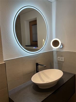 Ein modernes Badezimmer mit einem eleganten, runden Spiegel und einem stilvollen Waschbecken. Die Beleuchtung schafft eine gemütliche Atmosphäre.