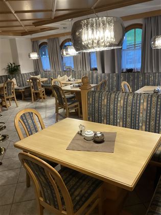 Ein gemütliches Restaurant mit Holztischen und -stühlen. Die Einrichtung ist stilvoll und entspannend, mit großen Fenstern und eleganten Leuchten.