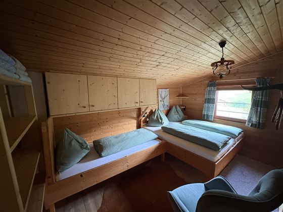 A cozy bedroom with wooden paneling and two beds. The windows offer a view of nature and the room has an inviting atmosphere.