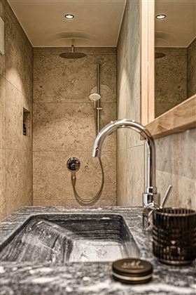 A modern bathroom with an elegant shower and a stylish stone sink. The walls are made of light stone, which gives the room a calm atmosphere.