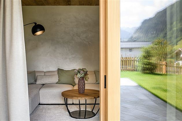 A modern living room with a comfortable couch and an elegant table. Large windows provide a view of the green meadow and the mountains.