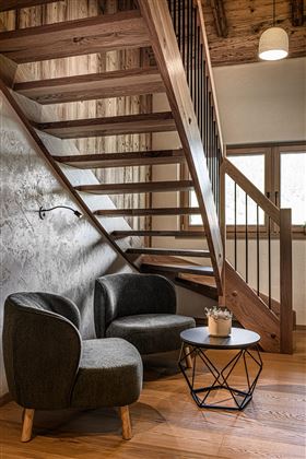A modern hallway with a wooden staircase and cozy armchairs. A small table with a plant completes the cozy atmosphere.