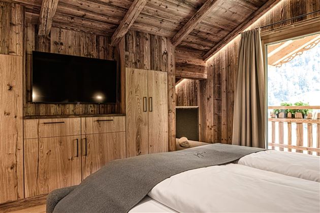A cozy bedroom with wood paneling and a large television. The large windows provide a view of the outdoors and let in plenty of light.